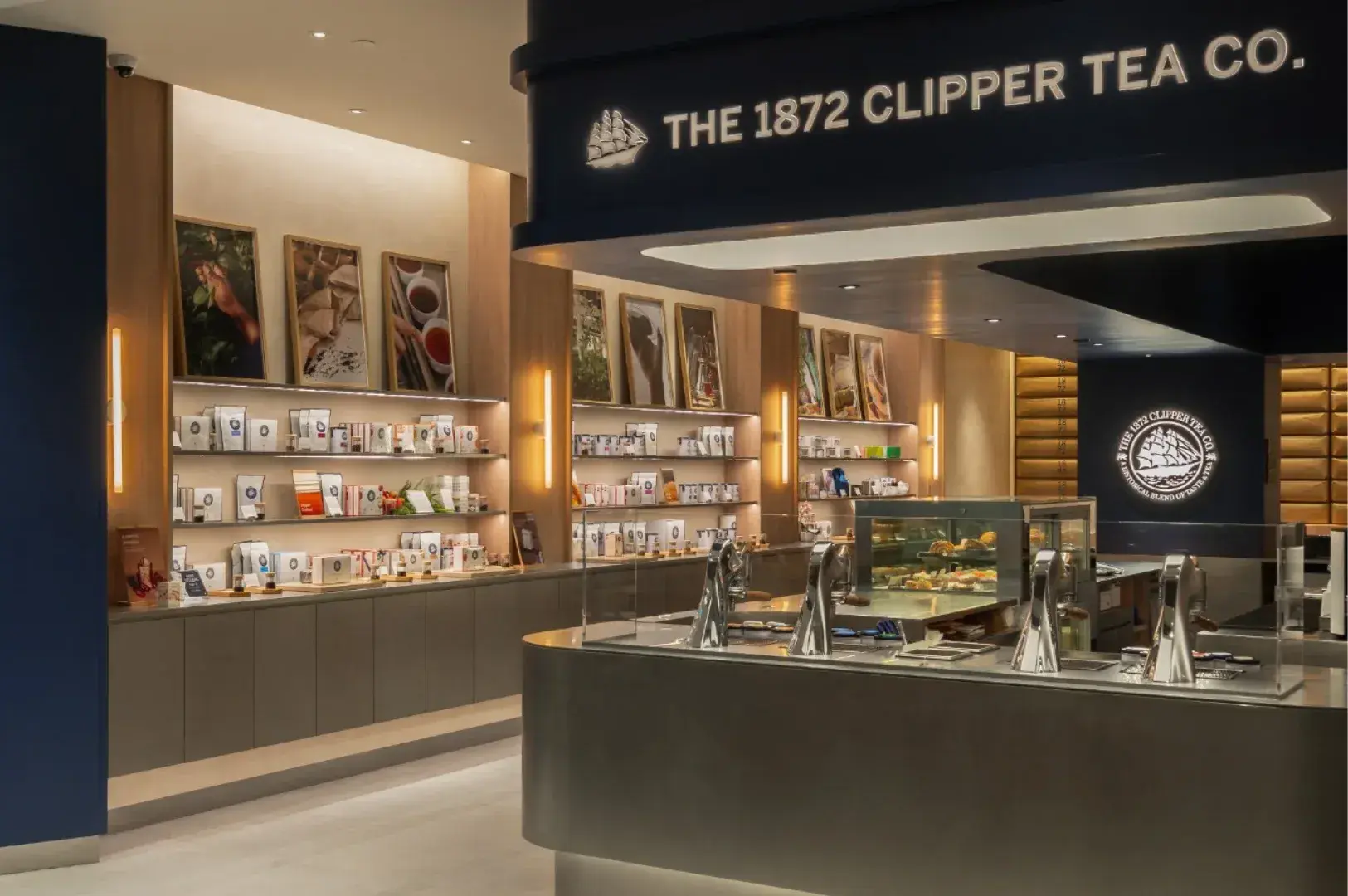 Storefront counter of "The 1872 Clipper Tea Co." retail kiosk with wall displays of packaged tea products and modern dispensing spouts.