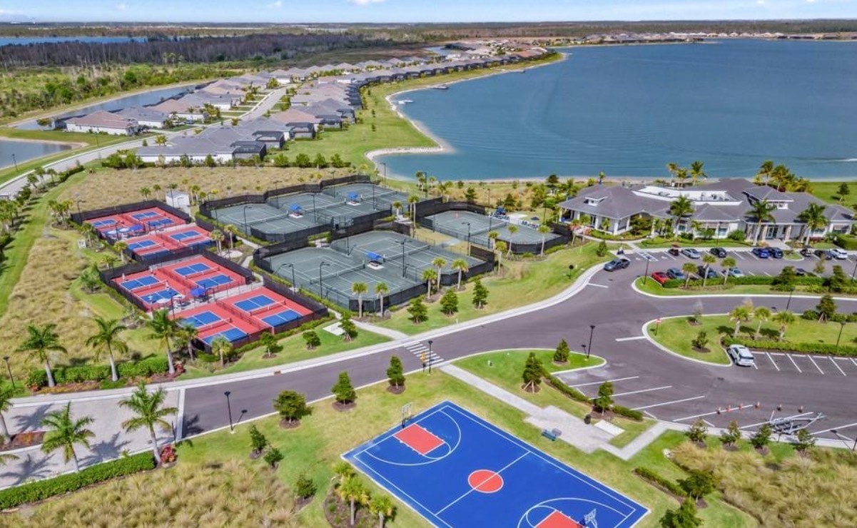 The image depicts a resort-style clubhouse featuring outdoor dining areas that overlook pristine lakes, embodying the lakefront lifestyle of the Wildblue community in Fort Myers, Florida. Surrounded by lush greenery and offering luxury amenities, this inviting space serves as a hub for residents to enjoy activities like paddle boarding and social gatherings.