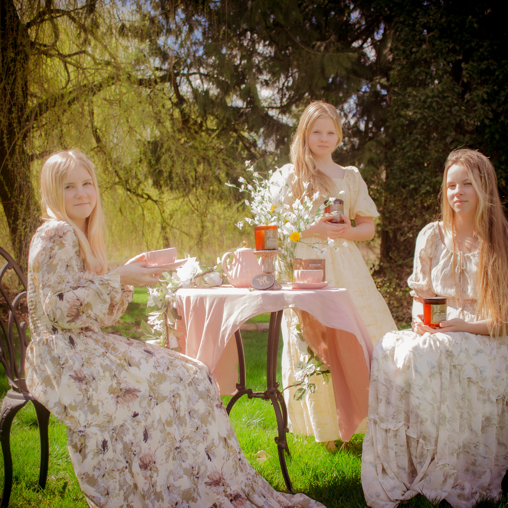 Three young ladies in pastel floral smock dresses having an outdoor tea party.