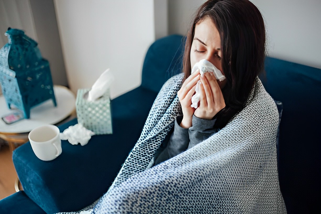 A photo of a woman sneezing covered by a blanket