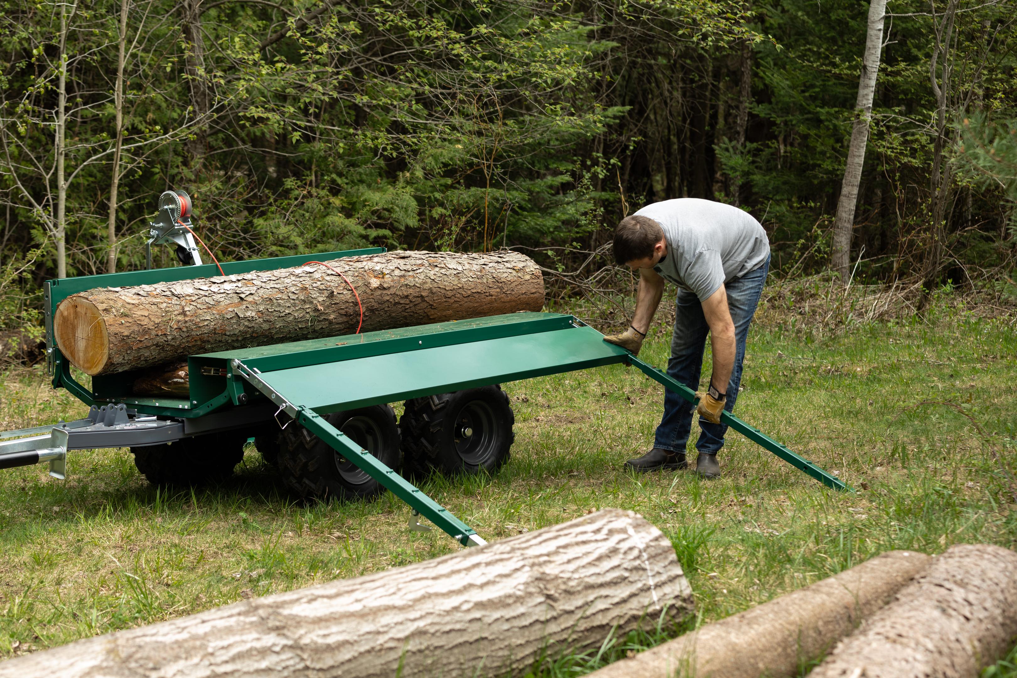 A person loading a log onto a Woodland Mills Multilander ATV Dump Trailer with a ramp.