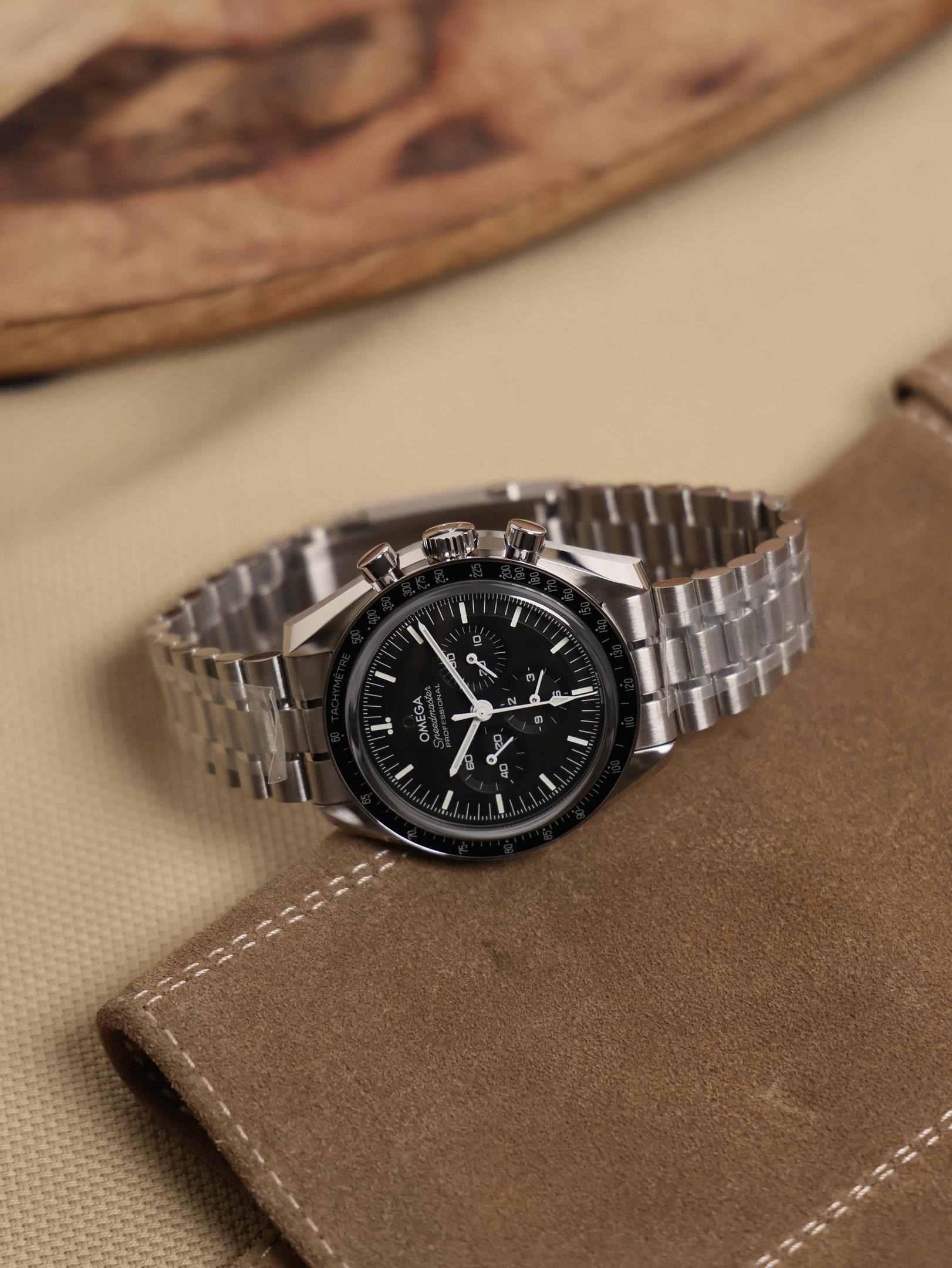 A luxury chronograph watch featuring a black dial and tachymeter bezel is elegantly displayed on a dark leather surface, illuminated by soft warm lighting. This timepiece embodies the quality and precision characteristic of Omega watches, making it a perfect addition to any men's watch collection.