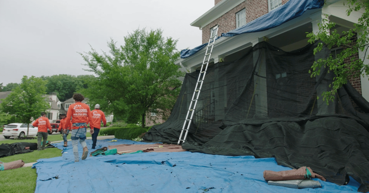 Team of Five Points Roofing contractors arriving with materials and tools, walking over fully tarped lawn at a Middle Tennessee roofing site.