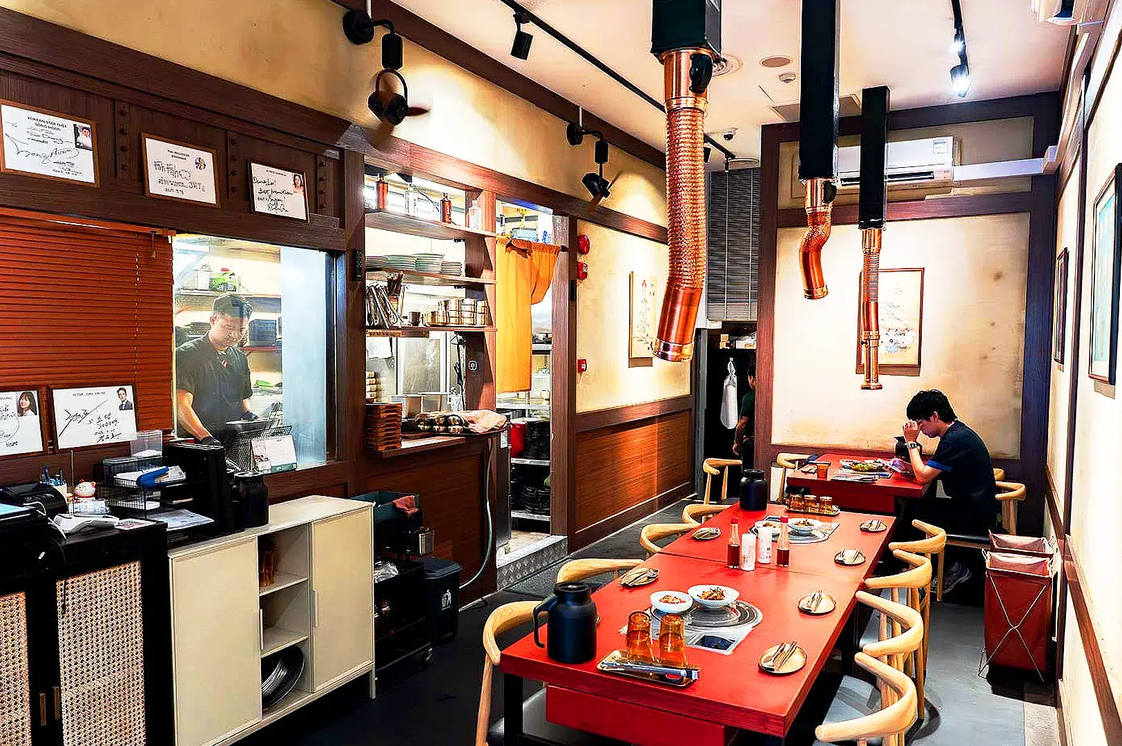 Traditional Korean restaurant interior with red dining tables, barbecue grills and copper exhaust hoods