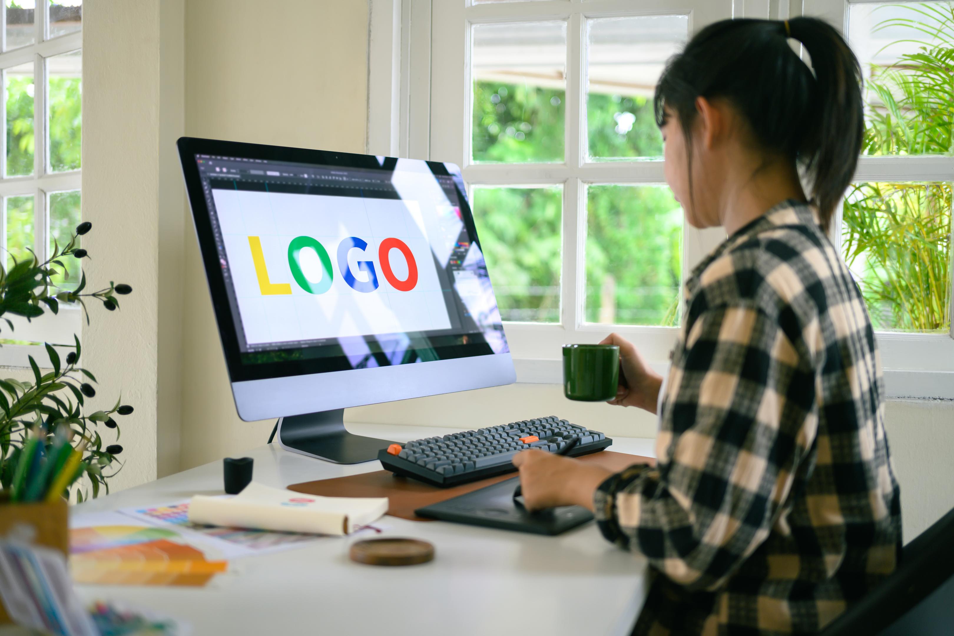 Jeune graphiste utilisant une tablette à stylet et un ordinateur pour concevoir un logo coloré