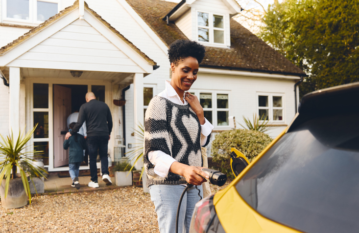 Woman charging an electric car parked in front of her house. 