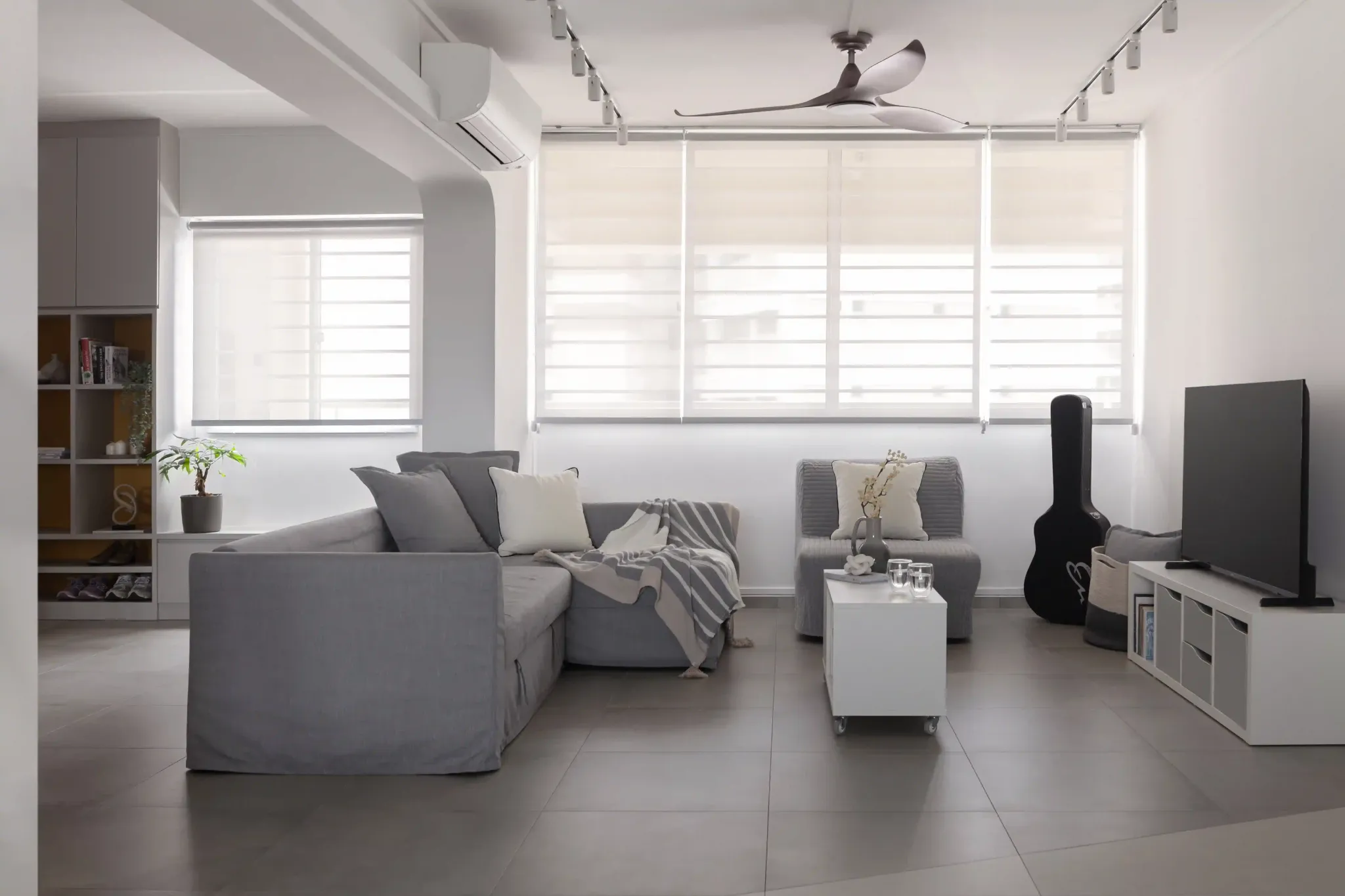 4 room HDB living room design with grey sectional, sheer blinds and track lights for a bright, flexible space.