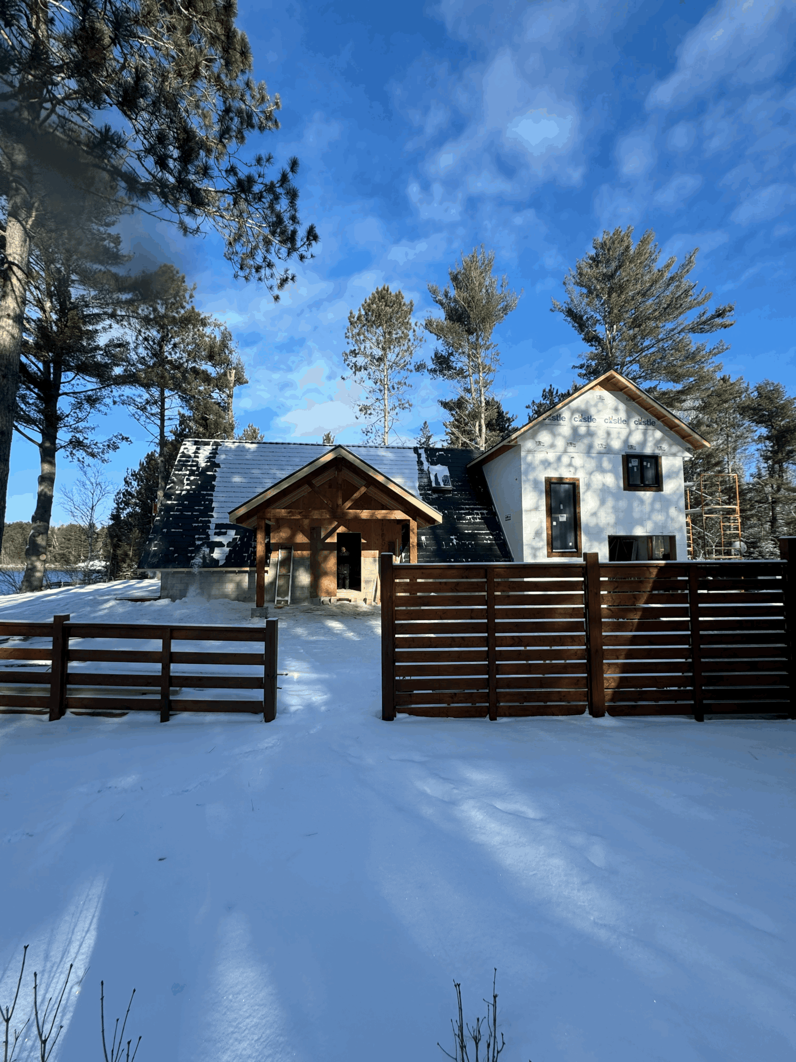 A snow-covered home with dark metal roofing, a fence and snow in the yard.