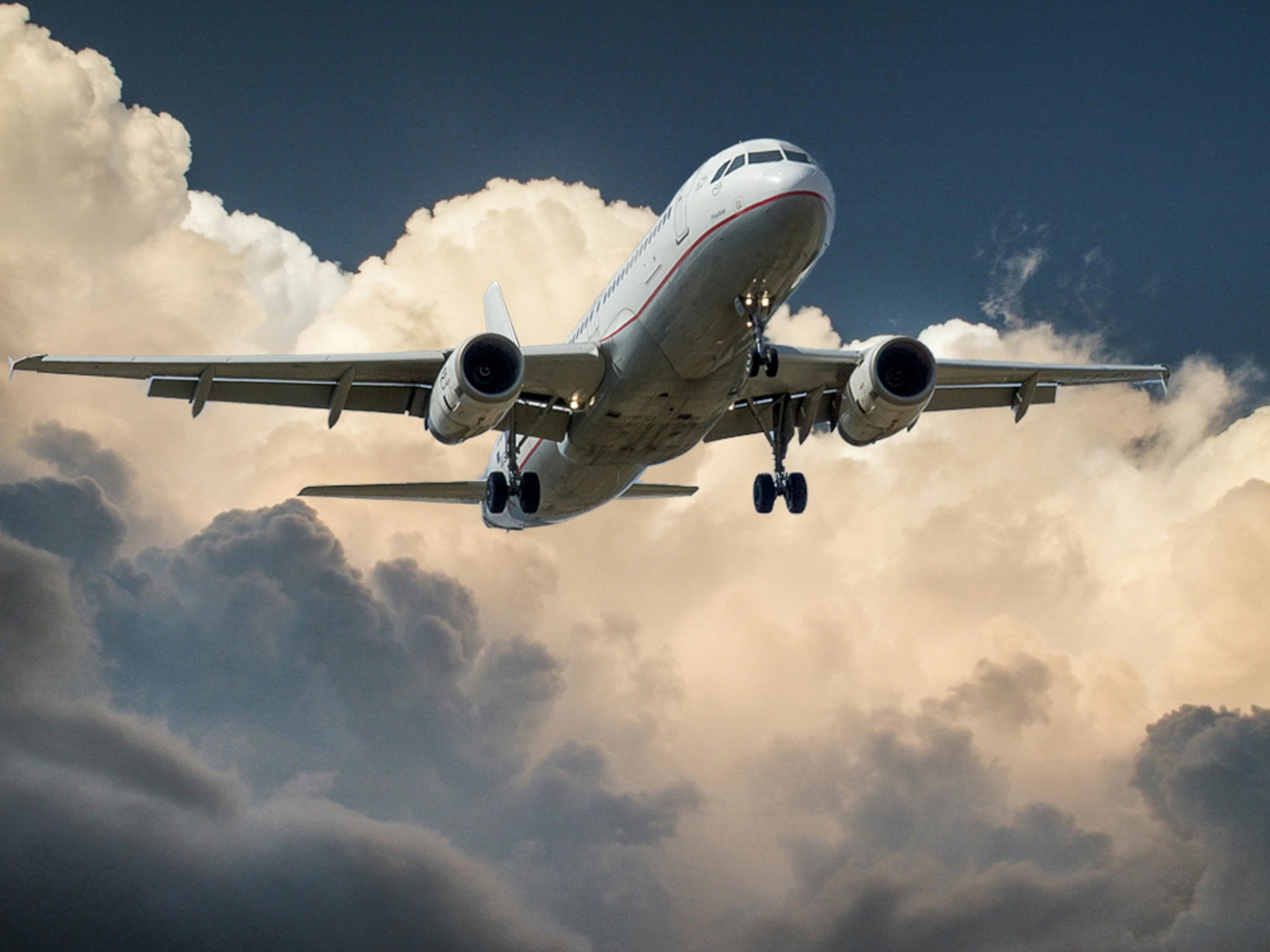 Commercial airplane flying through dramatic clouds with landing gear extended, captured from below against a moody sky.
