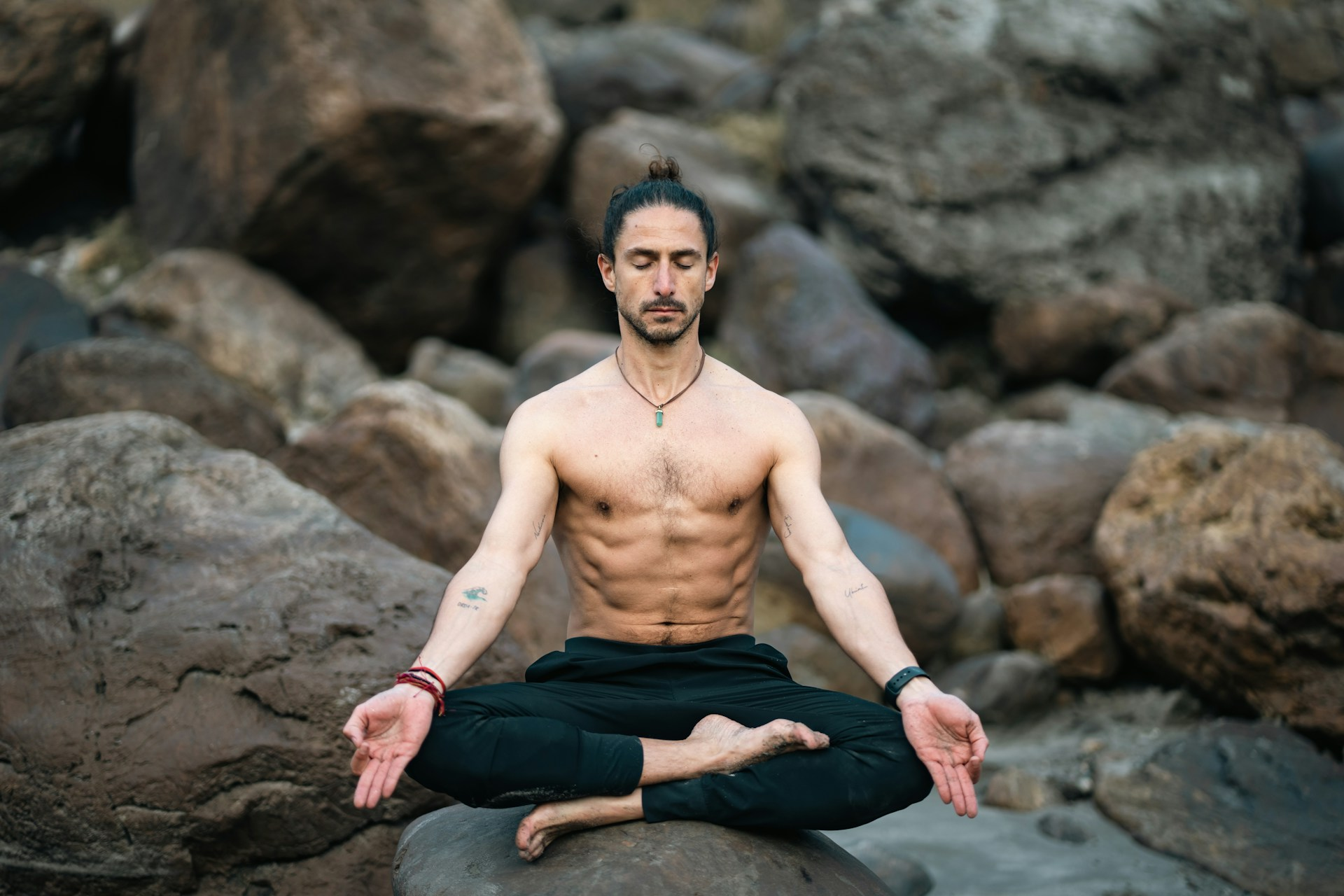 A man meditating on some rocks outside with his shirt off