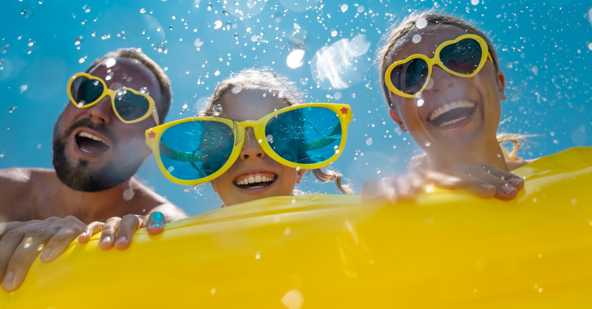 Family wearing sunglasses smiling and splashing in the pool at the Diplomat Wildwood during a sunny summer day.