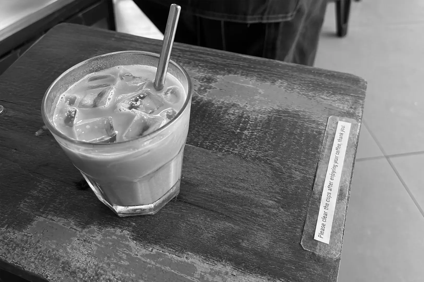 Glass of iced coffee with ice cubes and a metal straw on a rustic wooden café table.