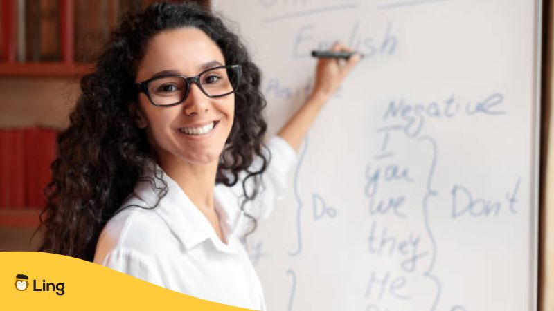 Excited woman in glasses looking at camera, writing on the board - How To Be A Good Language Teacher