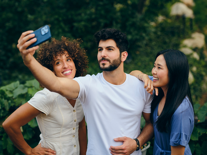 Three happy young adults snapping a selfie in front of some flowers. 