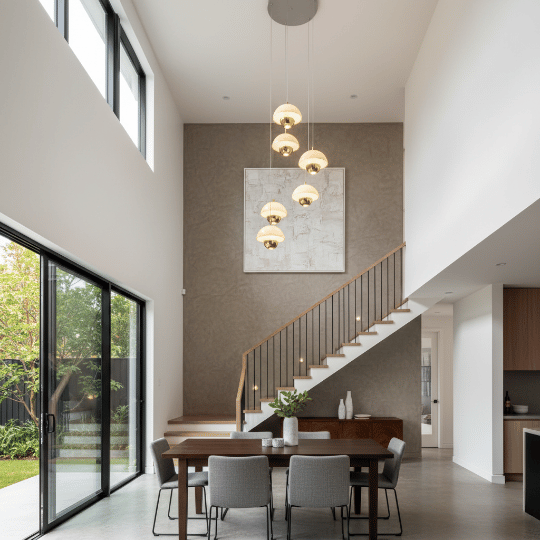 Stairwell pendant cluster with layered glass globes, adding statement lighting beside the dining table in a double-height space