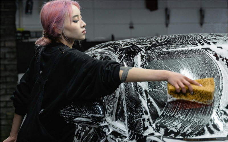 Person hand washing a black car with sponge and car wash soap during a car cleaning at home
