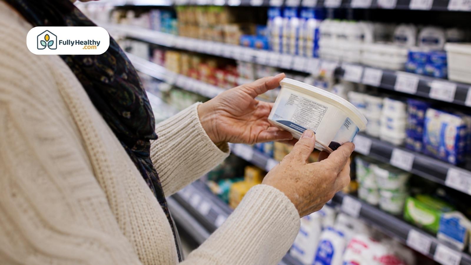 Shopper checking cream cheese nutrition label in a refrigerated grocery store aisle