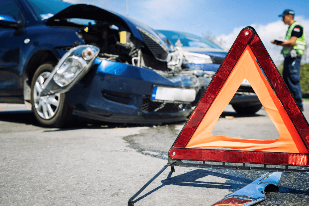 @Freepik, rawpixel.com | Wypadek samochodowy. Odmowa przyjęcia pomocy lekarskiej może spowodować utratę zdrowia. Rozbite auta i policjant. Trójkąt ostrzegawczy. Po wypadku auta są odcholowywane do miejsca docelowego - mechanika lub parking policyjny. 