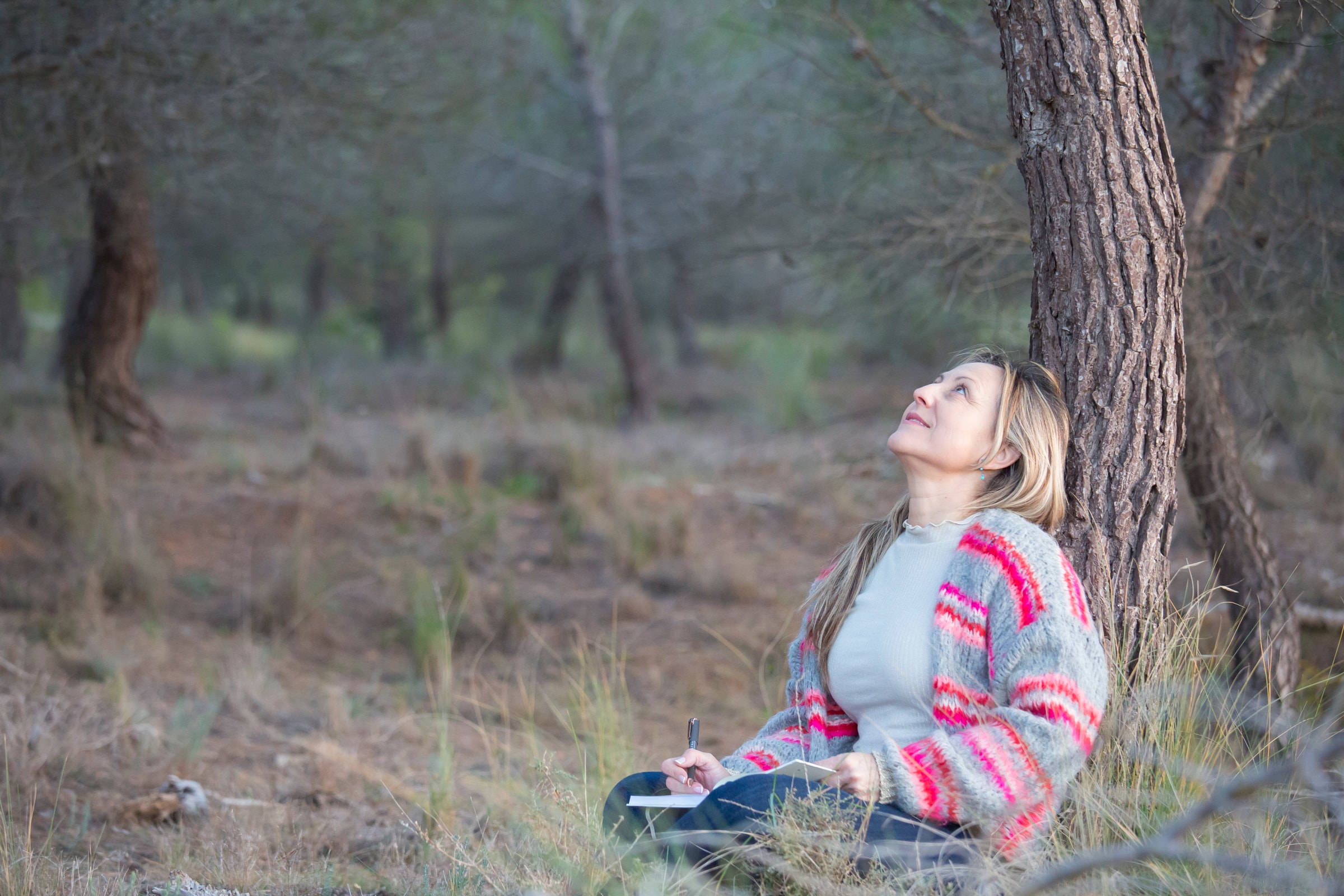 Nati Beltrán looking up leaning on a tree journaling