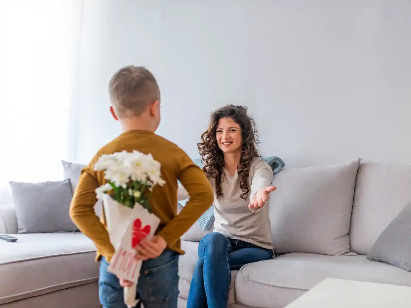 A young boy surprising his mother with a bouquet of white flowers, hidden behind his back. Fabulous Flowers and Gifts. Mother's Day Flowers.