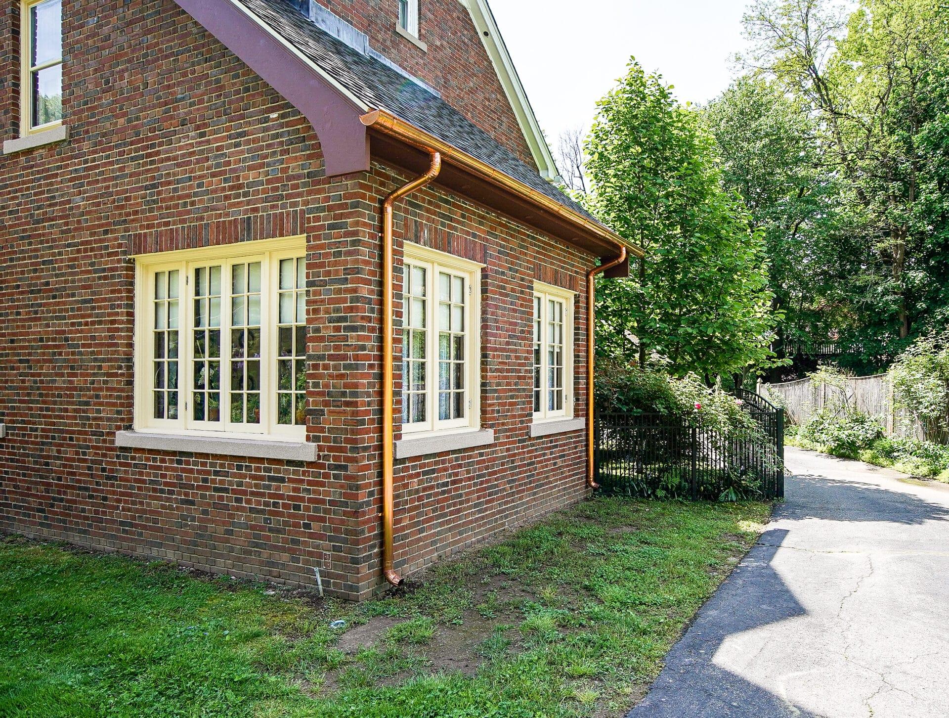 The image shows a traditional New England colonial style home featuring copper half round gutters that blend seamlessly with the architecture. These rust-resistant gutters are designed to handle heavy rain, ensuring proper drainage and preventing overflow while enhancing the home's curb appeal.