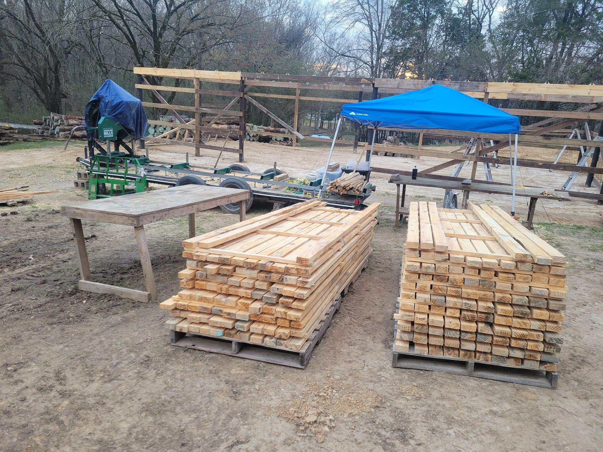 Une pile de planches sur un terrain, avec une scierie mobile Woodland Mills en arrière-plan.