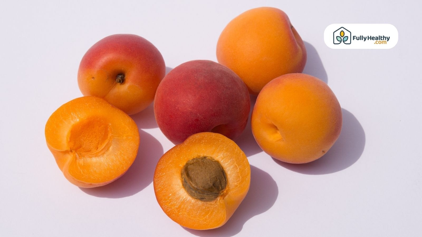 Whole and halved fresh apricots on a white surface with visible apricot seed
