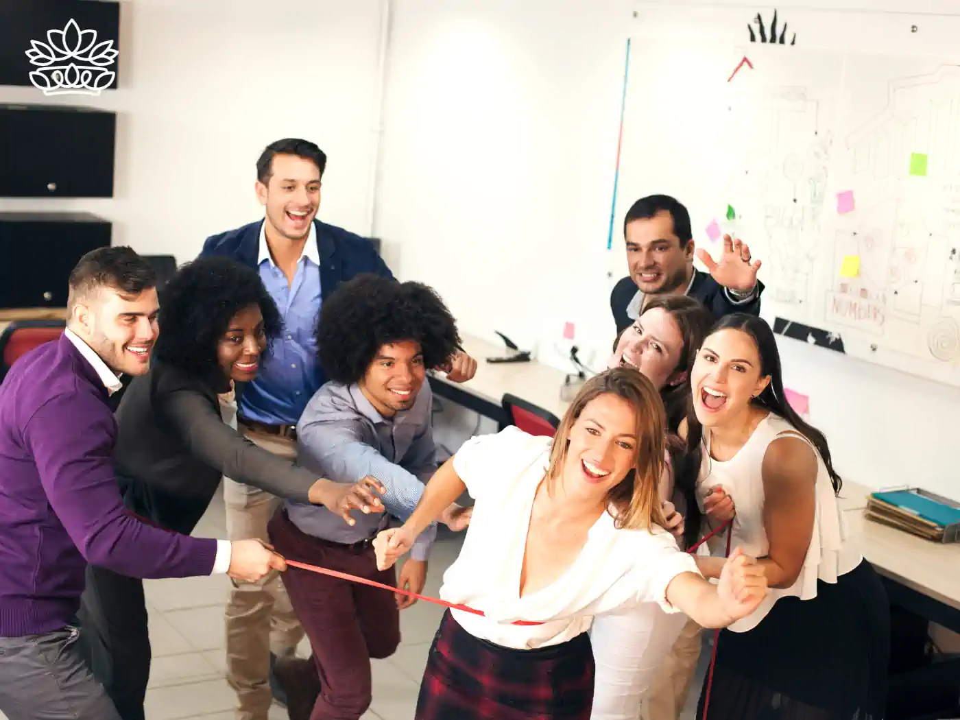 A vibrant and enthusiastic team of eight diverse office workers playfully engaging in a tug of war game, displaying teamwork and joy in a creative workplace setting. Fabulous Flowers and Gifts. Team Gifts. Delivered with Heart.