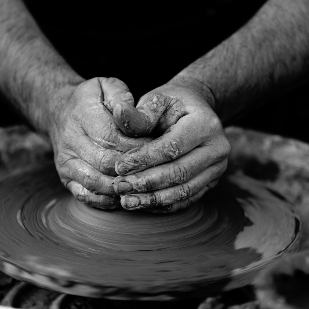black and white image of two hands at a pottery wheel