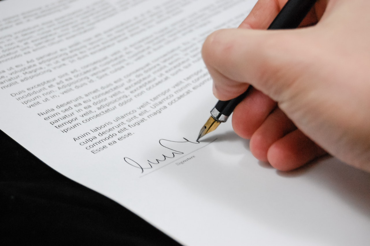 Hand met pen die contract ondertekent, focus op kleine lettertjes.