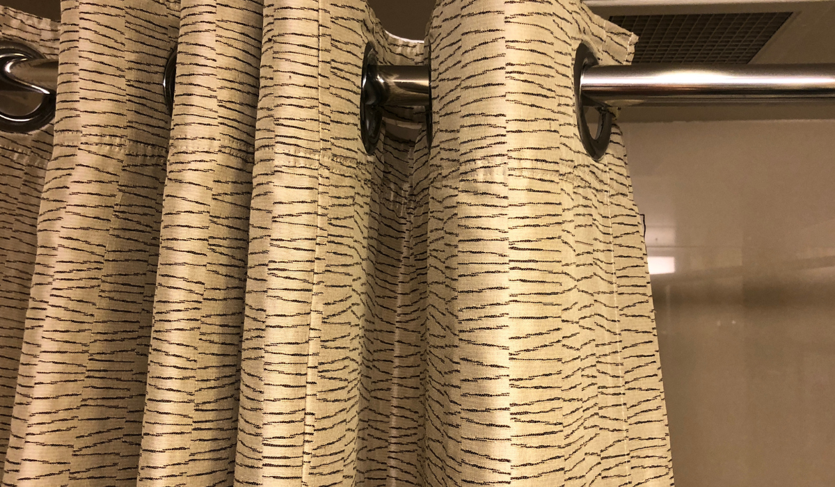 Shower curtain with large gromits close up on tension rod pole - bronze colour with fine black pattern
