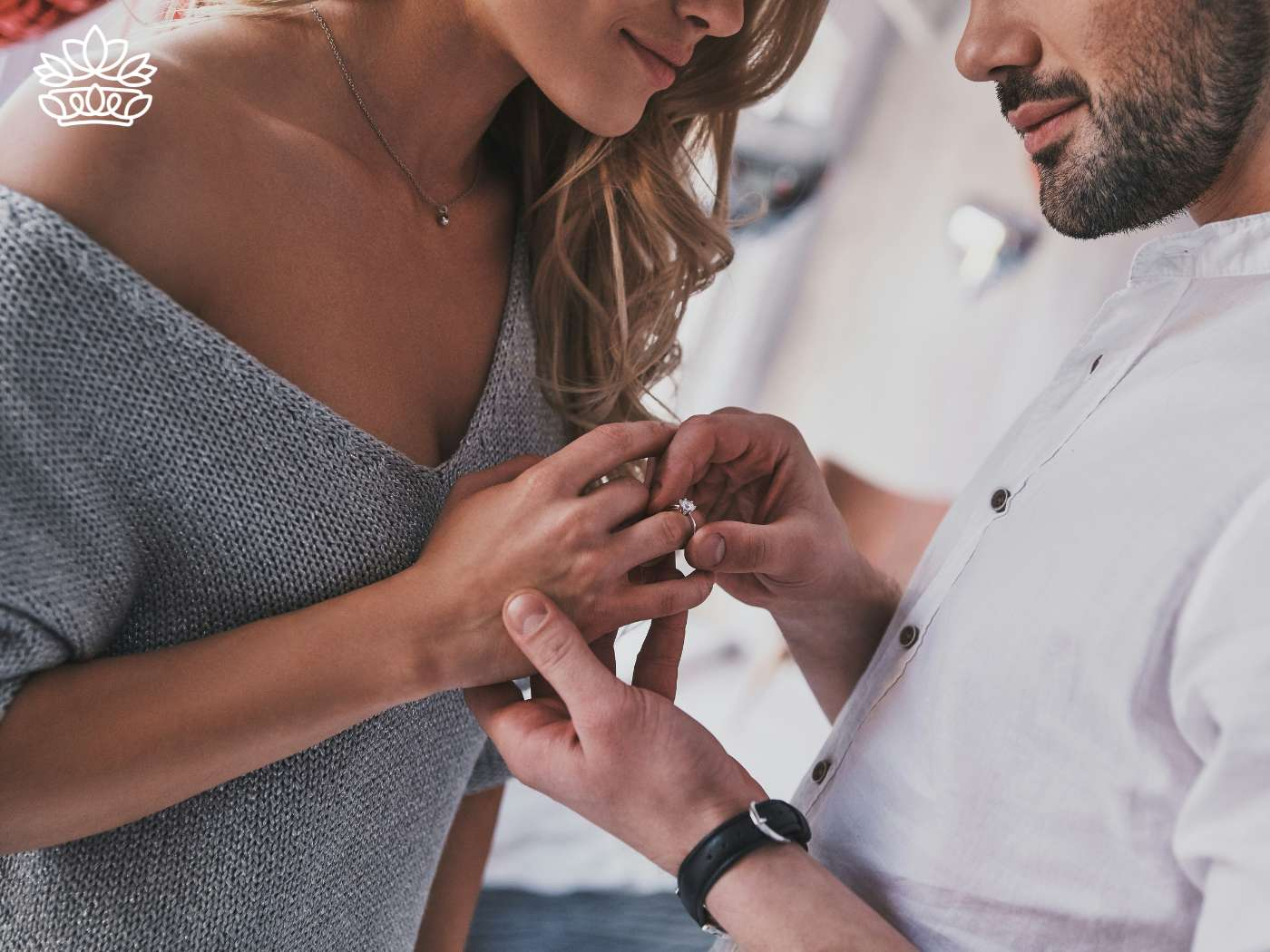 A close-up view of a man gently placing an engagement ring on a woman's finger, their intimate moment captured with warmth and affection. This beautiful engagement scene is complemented by the Engagement Gift Boxes Collection from Fabulous Flowers and Gifts, designed to celebrate such significant life events.