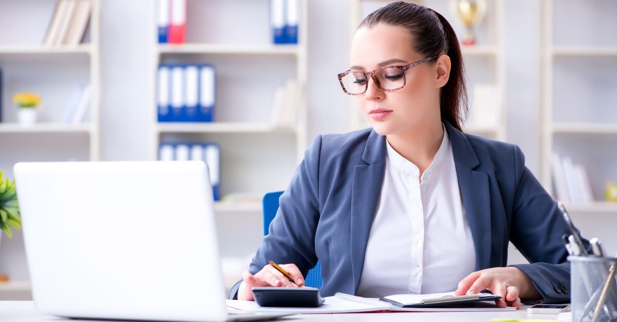 A professional accountant in a business suit working on tax basis accounting with a laptop and calculator.