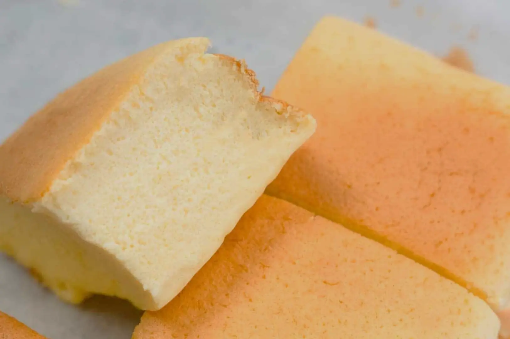A close-up of fluffy, light yellow cake squares with a slightly browned top. One square has a bite taken out of it.