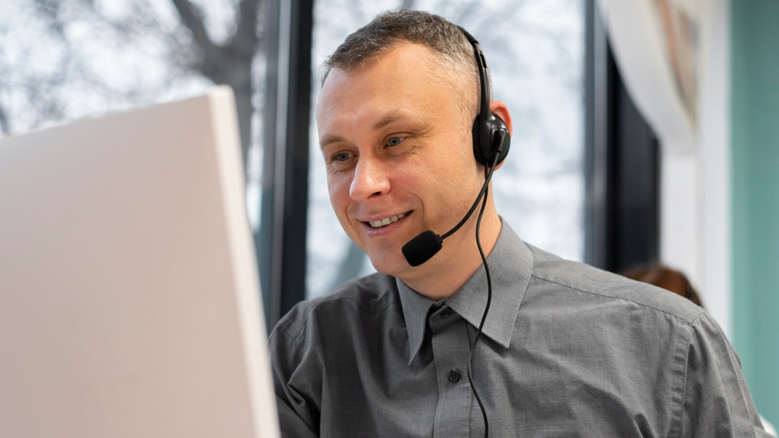 Customer support agent with headset smiling at screen, showing person-centered service that supports hybrid organizations.