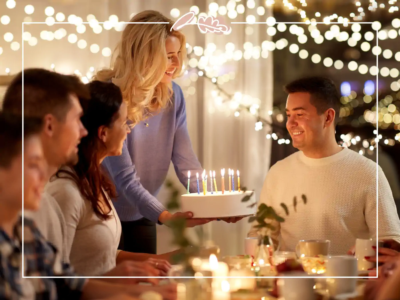 A group of friends celebrating a birthday with a cake lit by candles in a warmly lit room. Fabulous Flowers and Gifts.