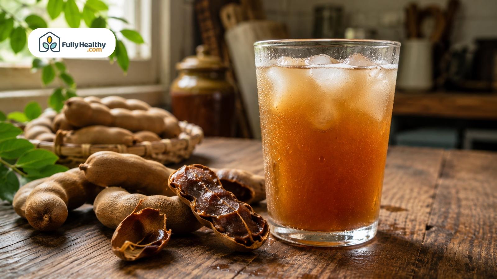 Chilled tamarind drink with ice served beside fresh tamarind pods on table