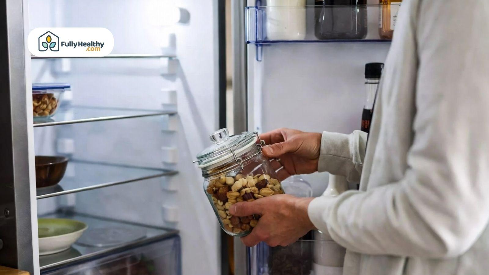 Person placing a glass jar of mixed nuts into an open refrigerator for storage.