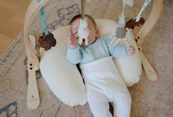 baby with a play gym laying on a nursing pillow