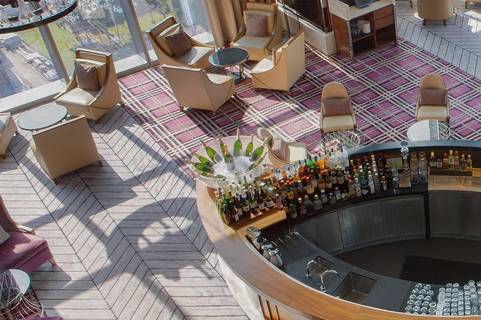 High-angle view of a curved bar counter and lounge with cream armchairs on plaid carpet.