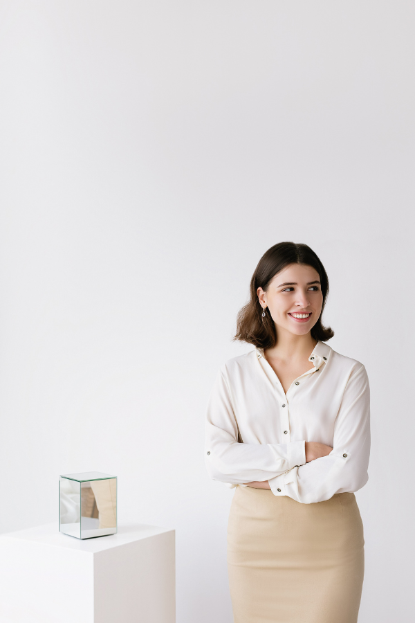 a young woman with a bob and pencil skirt stands next to an art pedestal