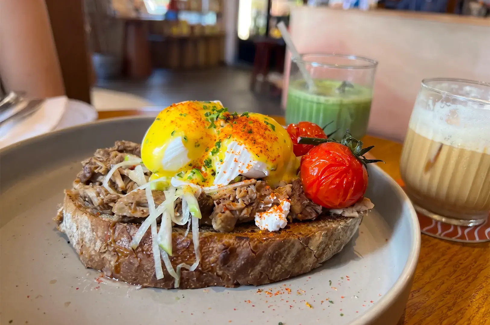 Five Oars Coffee Roasters signature Iberico Pork Eggs Benedictserved on a white plate on a wooden table.