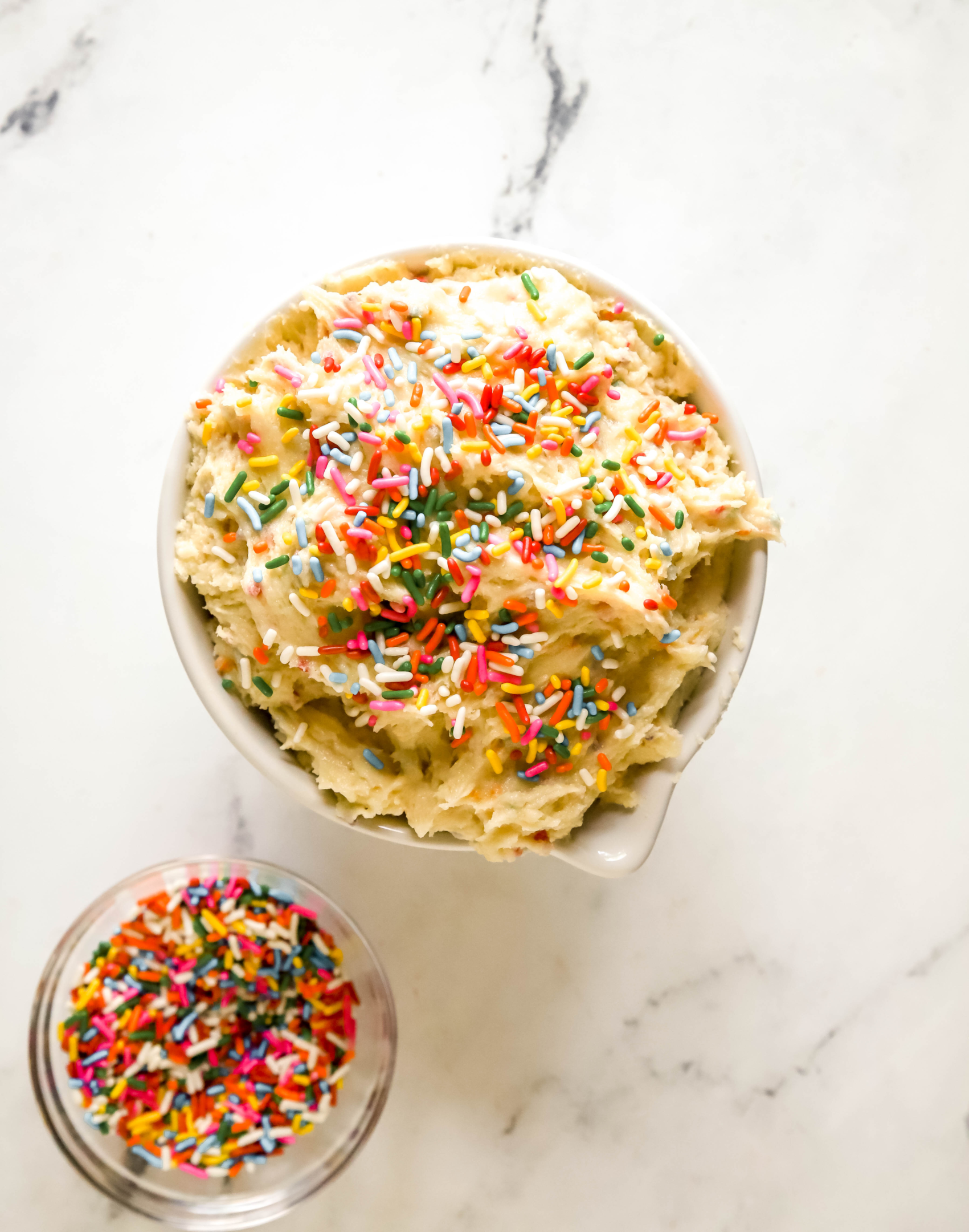bowl of cake batter dip topped with rainbow sprinkles and a bowl of rainbow sprinkles next to it