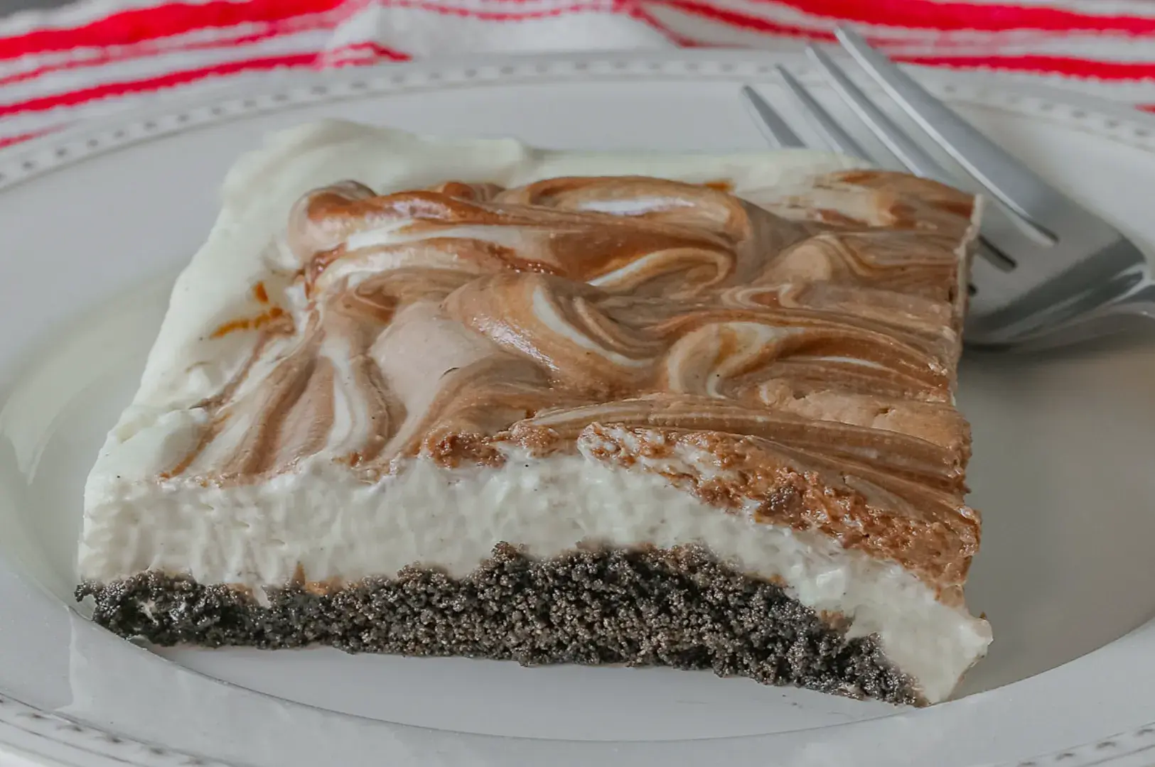 A slice of a dessert with a creamy white base and chocolate swirls, sitting on a plate with a fork beside it.