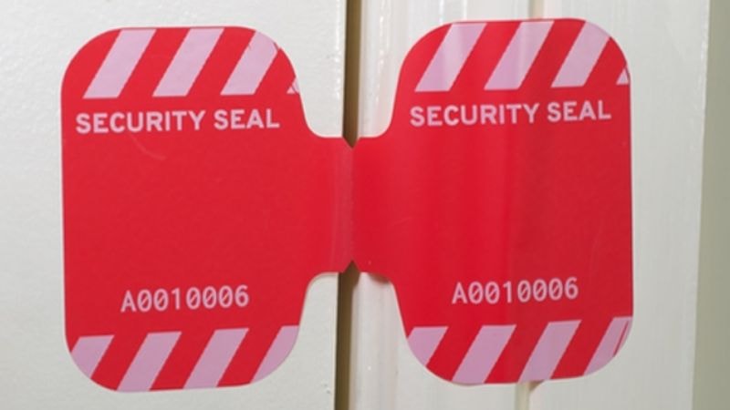 Tamper-evident red security label displaying unique identifier 'A0010006' on white surface