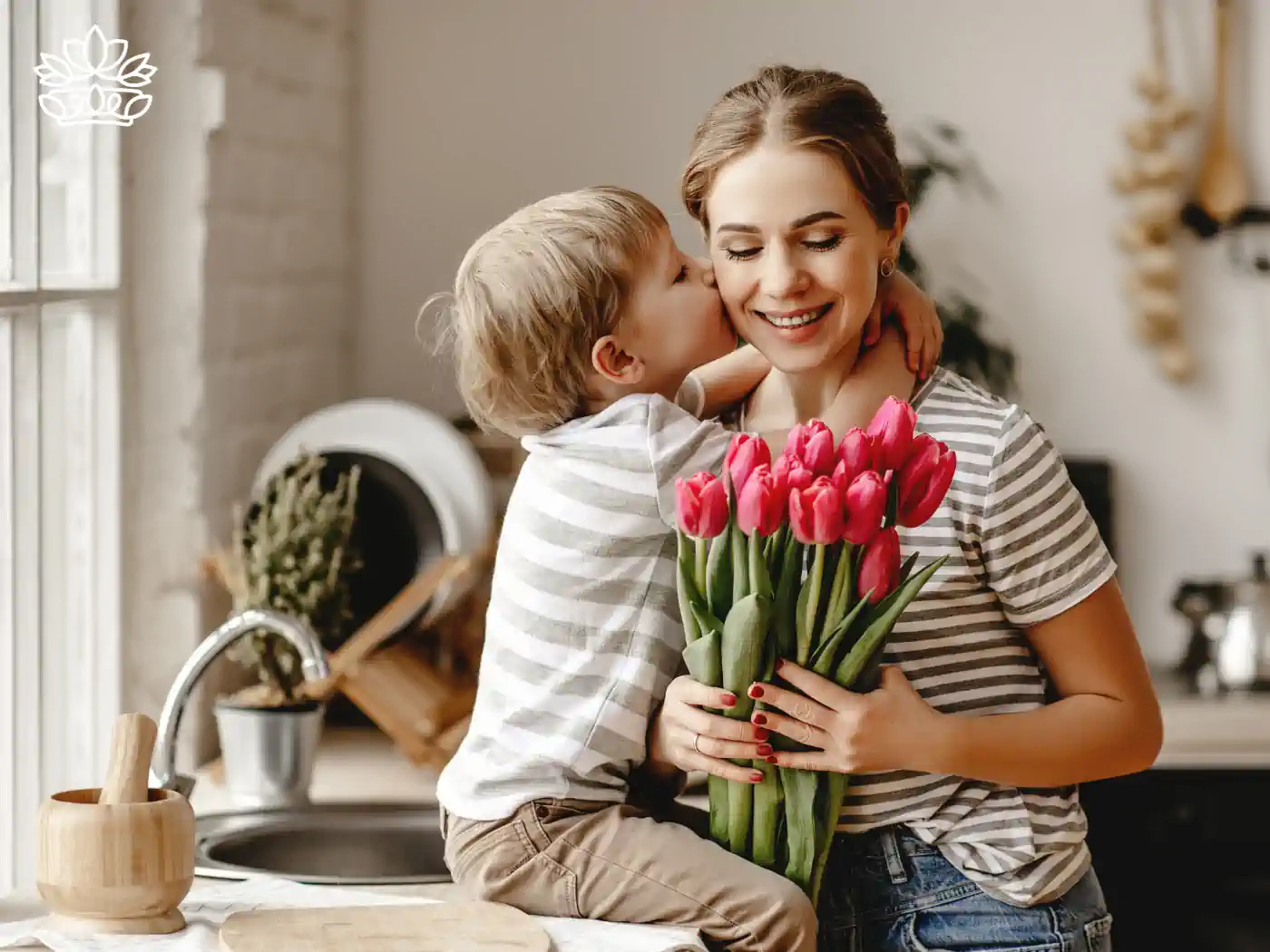 Image of a young boy kissing his mother's cheek while she holds a bouquet of tulips in the kitchen. Fabulous Flowers and Gifts - Luxury Flower Bouquets.