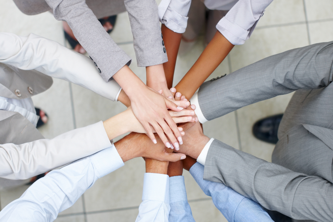 Diverse remote team stacking hands to show collaboration and unity