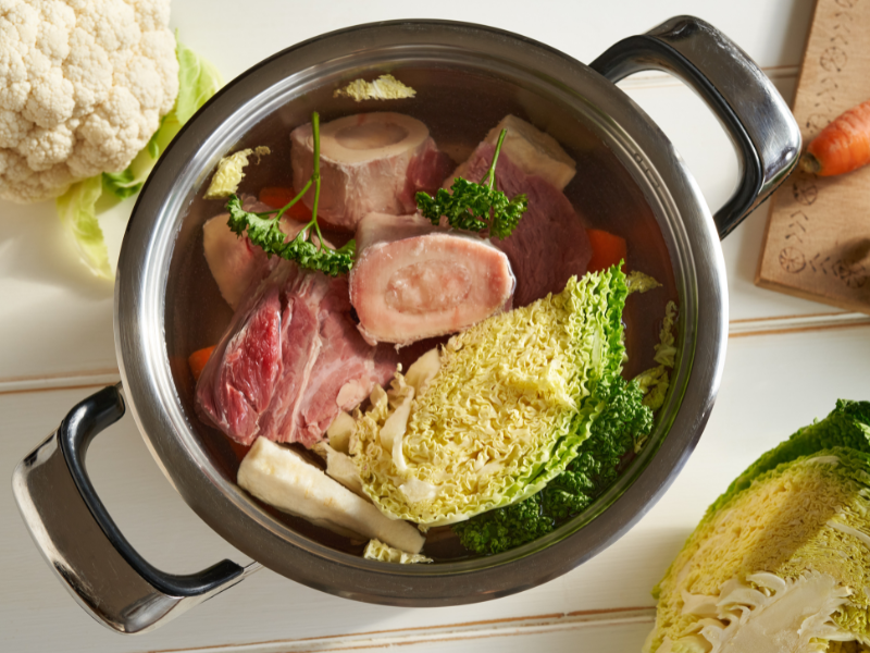 An image showing a bowl of bone broth with animal bones and vegetables.