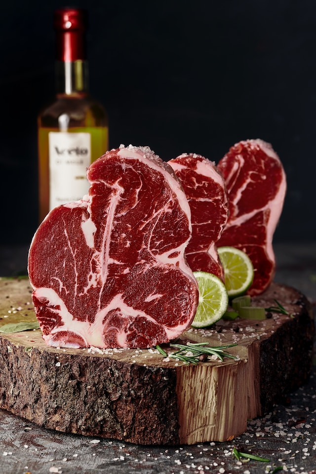 2 T bone steaks upright on a wooden tree platter with a bottle of of wine in the background