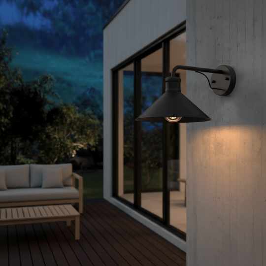 Black barn light wall sconce mounted beside sliding glass doors on a modern outdoor deck at night.